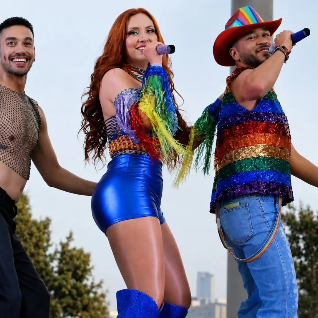 Vocalista pelirroja con bailarines vestidos de arcoíris